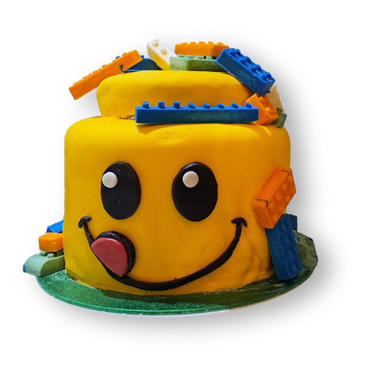 It is a cake with the shape of a lego head. The head is sticking its tongue out and it has chocolate legos all over it.